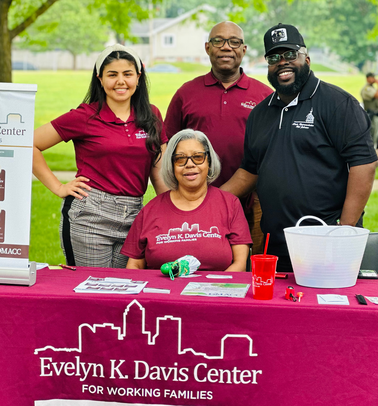 Three people stand behind a table with a cloth reading "Evelyn K. Davis Center for Working Families." A woman sits at the table.