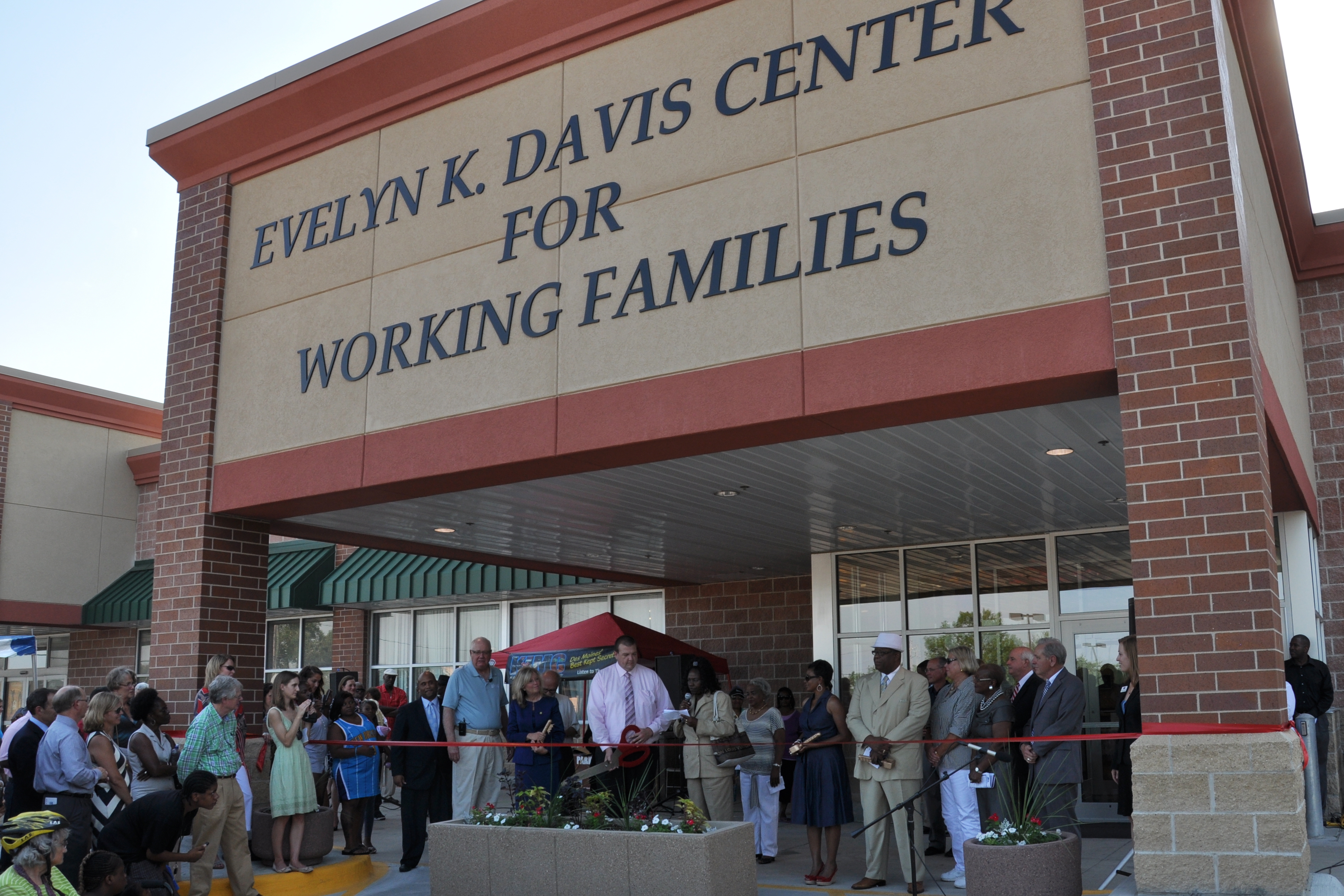 A crowd stands below a building with a sign reading "Evelyn K. Davis Center For Working Families" while a long red ribbon is cut.