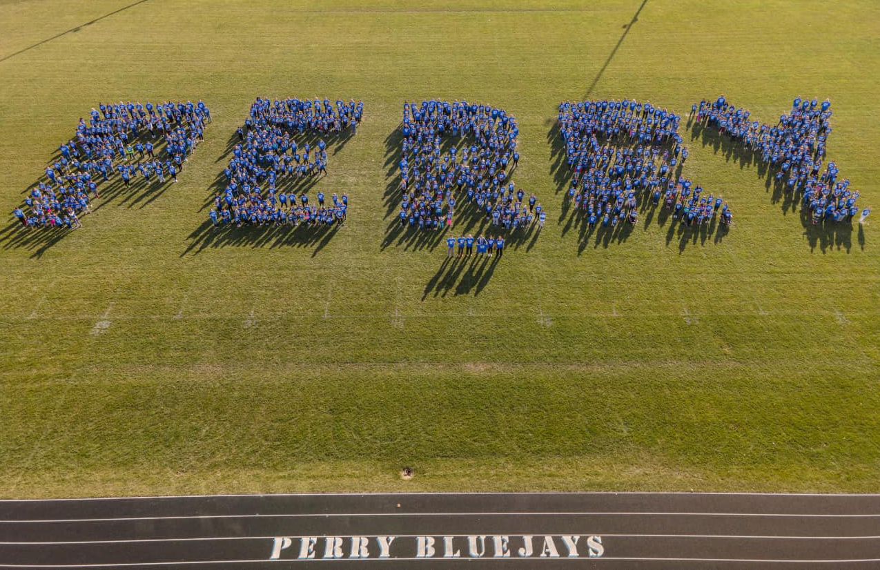 Upon his arrival in Perry on Dec. 7, 2023, U.S. Secretary of Education Dr. Miguel Cardona​​ is greeted by nearly 800 students from Perry Elementary School, who stood together to spell PERRY on the district's football field. Dr. Cardona (above, in front row) was delighted by the creative and enthusiastic welcome and joined the elementary school students, as well as their teachers and school administrators, for a group photo celebrating the school's 2023 National Blue Ribbon Schools Award.